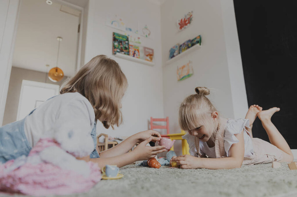 Dzieci bawią się kolorowym plastikowym zestawem do herbaty. Dzieci leżące na dywanie w domach w słonecznej, białej sypialni lub przedszkolu. Zabawna edukacja ekologiczna gra dla dzieci. Przestrzeń kopiowania - Zdjęcie, obraz