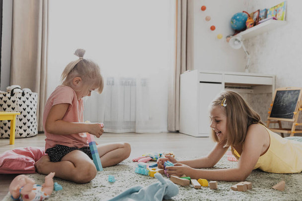 Діти грають з барвистими іграшками. Діти сидять на килимі вдома в спальні або дитячому садку, дитячій. Освітня екологічна гра для дітей. Чарівні маленькі дівчата будують будинок, вежу разом - Фото, зображення