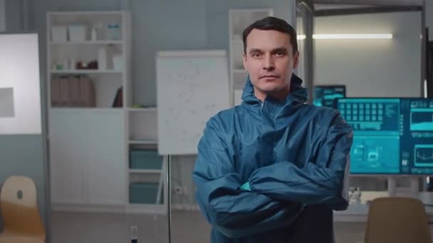 Mittleres Porträt eines ernsthaften kaukasischen Wissenschaftlers in Schutzanzügen oder Kamera mit gefalteten Händen stehend im modernen Forschungslabor - Filmmaterial, Video