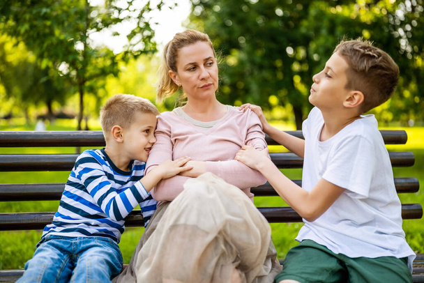 Matka siedzi z synami na ławce w parku. Jest zła, a chłopcy próbują przeprosić.. - Zdjęcie, obraz