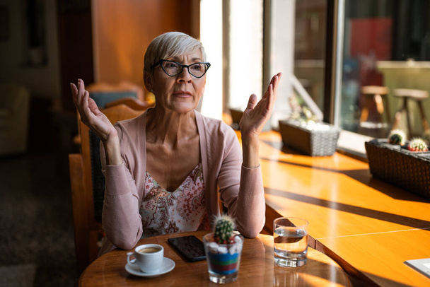 Olgun kadın kafede kahve içiyor. Garson servisinden memnun değil.. - Fotoğraf, Görsel