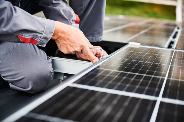 家の屋根に太陽光発電の太陽電池パネルを取付ける人間の技術者. ヘックスキーの助けを借りてソーラーモジュールシステムをインストールするマウントのクローズアップビュー. 代替エネルギー,再生可能エネルギーの概念. - 写真・画像