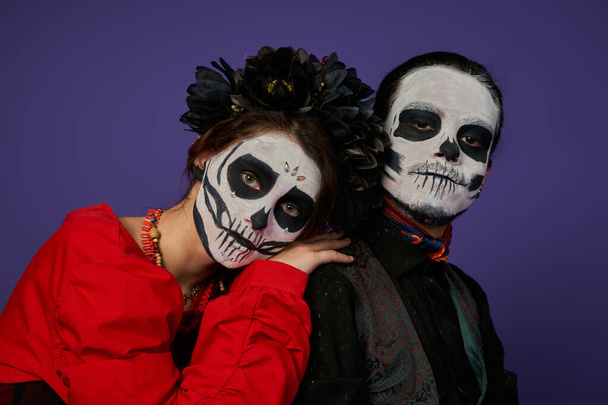 woman in sugar skull makeup and black wreath leaning on shoulder of eerie man on blue, Day of Dead - Photo, Image