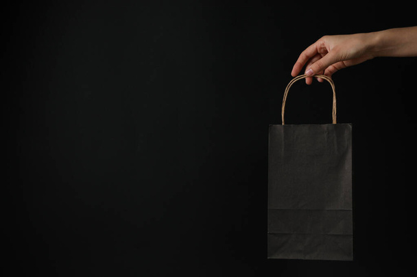 Paper shopping bag in hand on black background. - Photo, Image