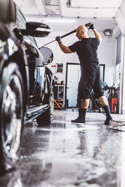 Обслуговуючий чоловік миє машину перед деталізацією в майстерні. Професійна робота - Фото, зображення
