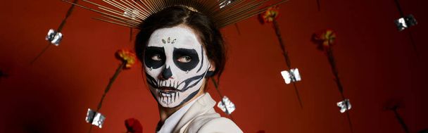 mujer aterradora en día de los muertos maquillaje de cráneo de azúcar mirando hacia otro lado sobre fondo floral rojo, pancarta - Foto, Imagen