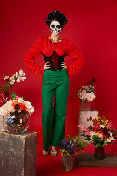 kobieta w makijażu czaszki cukru w pobliżu tradycyjnej dia de los muertos ofrenda z jasnymi kwiatami na czerwono - Zdjęcie, obraz