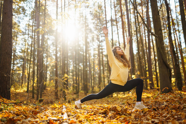 An active woman in sportswear performs yoga exercises in the autumn forest on fallen leaves, catches zen, meditation, relaxation. The concept of relaxation, freedom. - Foto, Imagen