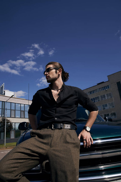 plan vertical de l'homme sexy élégant avec des lunettes de soleil et montre-bracelet posant près de la voiture et regardant loin - Photo, image