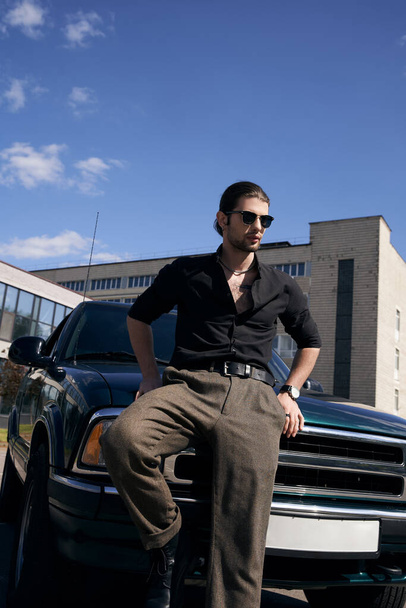 mladý stylový muž v černém ležérní oblečení stojí vedle svého zeleného auta a dívá se jinam, móda - Fotografie, Obrázek