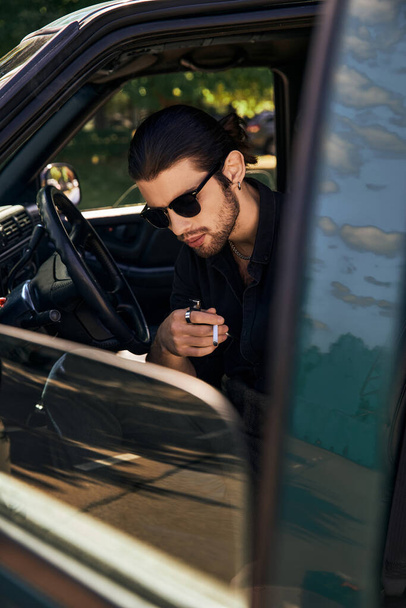bellissimo uomo sexy con occhiali da sole e coda di cavallo rilassante dietro il volante con sigaretta in mano - Foto, immagini