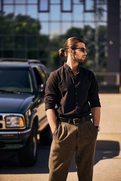 accattivante giovane uomo con accessori posa accanto alla sua auto con le mani in tasca, autista sexy - Foto, immagini