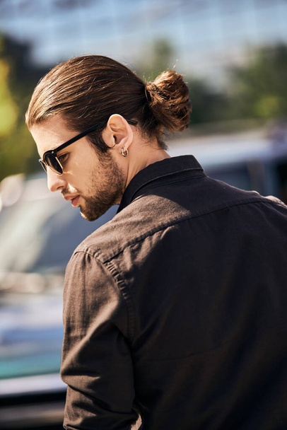 knappe jongeman met zonnebril en oorbel poserend in profiel bij zijn auto, mode en stijl - Foto, afbeelding