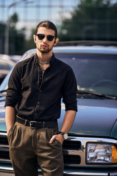 привлекательный элегантный мужчина модель в черной стильной рубашке с руками в карманах, глядя на камеру, мода - Фото, изображение