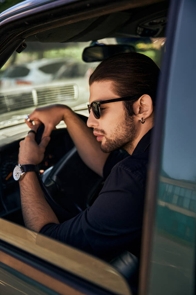 modelo masculino jovem na moda com olhar dapper sentado atrás do volante de seu carro, motorista sexy - Foto, Imagem
