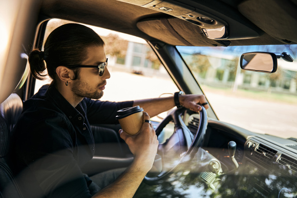 przystojny mężczyzna z kucykiem za kierownicą jego samochodu z kawą w ręku, sexy kierowca - Zdjęcie, obraz