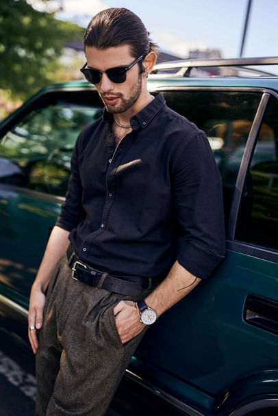 homem sexy elegante em camisa preta com óculos de sol posando ao lado de seu carro ao ar livre, moda e estilo - Foto, Imagem