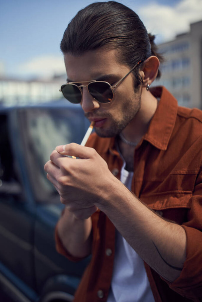 πορτρέτο του νεαρού κομψό άνδρα με γυαλιά ηλίου ανάβει το τσιγάρο του, κάθετη, στυλ έννοια - Φωτογραφία, εικόνα