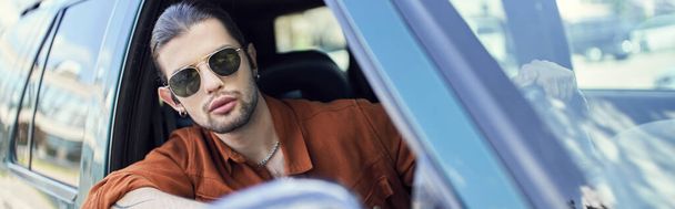 good looking stylish man in brown shirt looking out of car window, fashion concept, banner - Photo, Image