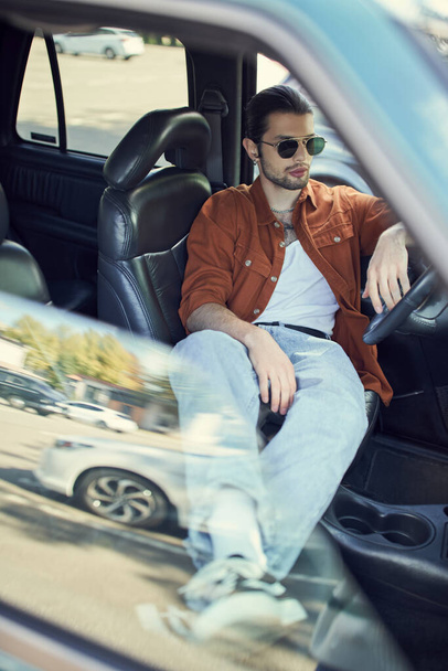 modelo masculino elegante joven en camisa marrón que se enfría detrás del volante de conducción, concepto de moda - Foto, Imagen