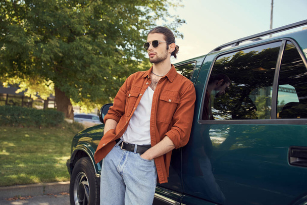 buen aspecto modelo masculino con aspecto elegante posando junto a su coche con las manos en los bolsillos, conductor sexy - Foto, Imagen