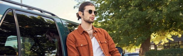 όμορφος σέξι άντρας με καφέ πουκάμισο και τζιν που ποζάρει δίπλα στο αμάξι του, μόδα, λάβαρο - Φωτογραφία, εικόνα