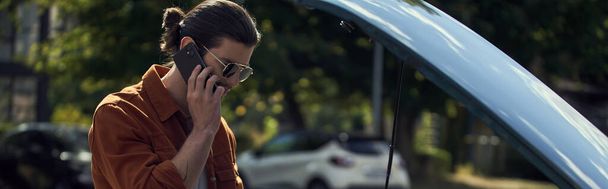 Şık bakışlı ve güneş gözlüklü yakışıklı genç adam sigortacısıyla telefonla, afişle konuşuyor. - Fotoğraf, Görsel
