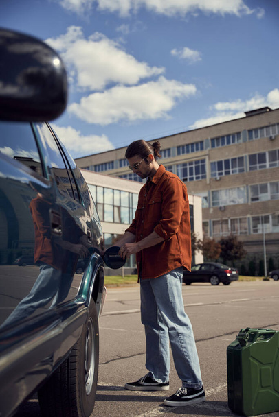 vertical shot of attractive male model in stylish brown shirt refueling his car with petrol - Photo, Image