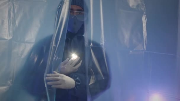 Colpo medio di giovane scienziato maschio Biracial in indumenti protettivi utilizzando torcia sul suo smartphone durante l'esame zona rossa del laboratorio scientifico - Filmati, video
