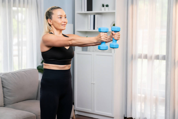 Athletic and sporty senior woman engaging in body workout routine with lifting dumbbell at home as concept of healthy fit body with body weight lifestyle after retirement. Clout - Photo, Image