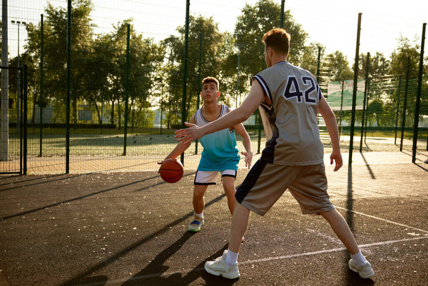 Aktiivinen isä ja teini poika pelaavat koripalloa katukentällä. Urheilu ja harrastus virkistys perheelle viikonloppuna - Valokuva, kuva