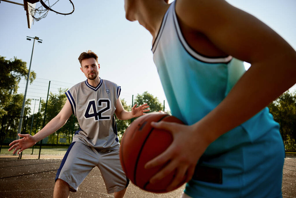 A teenager boy preparing to throw ball into basket hoop. Happy dad and son playing basketball on outdoor street court - Photo, Image