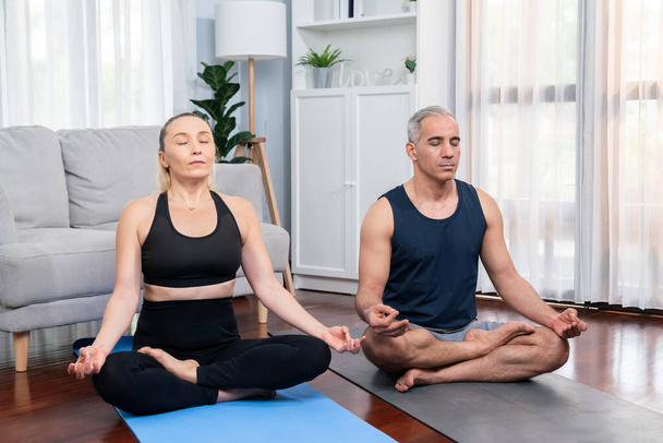 Glückliches, aktives Seniorenpaar in Sportkleidung, das zu Hause Yoga in Meditationshaltung auf der Trainingsmatte macht. Gesunder Senioren-Lebensstil mit friedlichem Geist und Gelassenheit. Schlagkraft - Foto, Bild