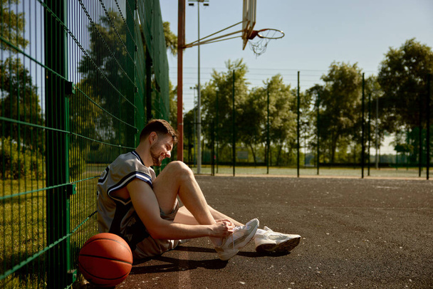 Sportif attachant des lacets sur des baskets assises sur un terrain de basket. Préparation pour le match - Photo, image