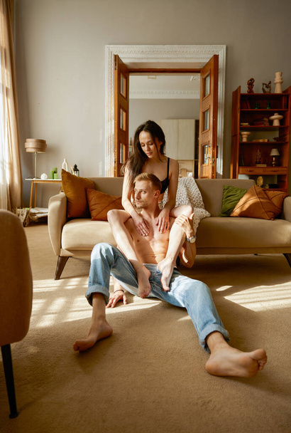 Erotický napůl oblečený pár odpočívá spolu doma v obýváku. Mladá atraktivní přítelkyně dává nohu na rameno přítele. Snění lidé emoce a romantický vztah - Fotografie, Obrázek