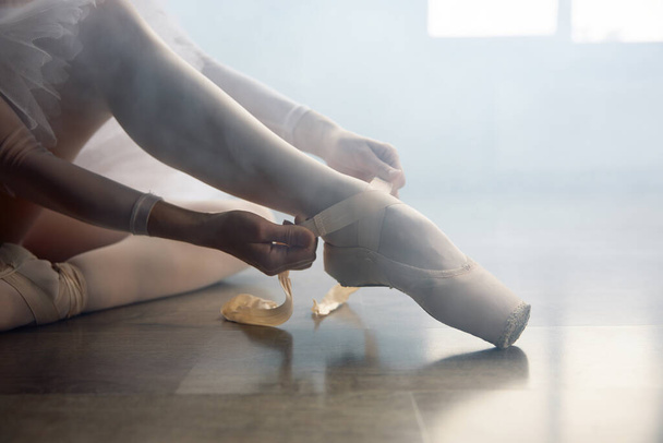 Ballerina sedí na podlaze a před hodinou choreografie si obléká špičaté boty. Krásná tanečnice se připravuje na vystoupení nebo trénink na taneční škole - Fotografie, Obrázek