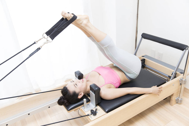 sporty Japanese woman in sportswear training with reformer indoors - Foto, imagen