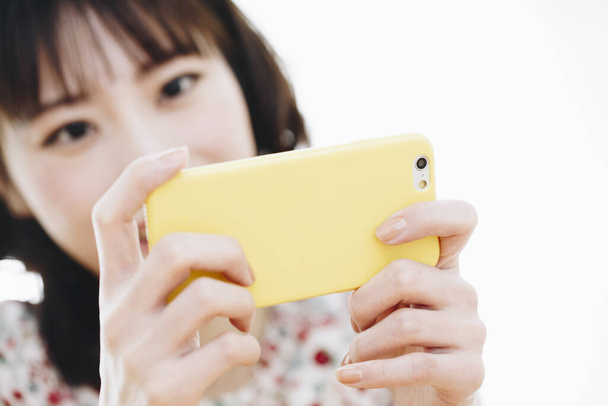 Beautiful young Asian woman using smartphone at home - Фото, изображение