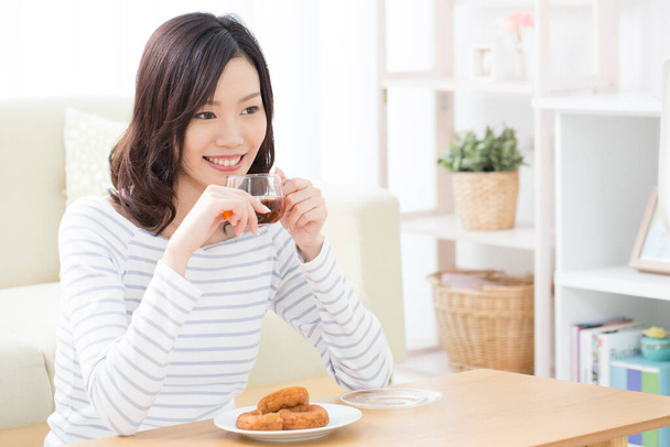 young Japanese woman drinking tea from glass mug at home - Foto, afbeelding