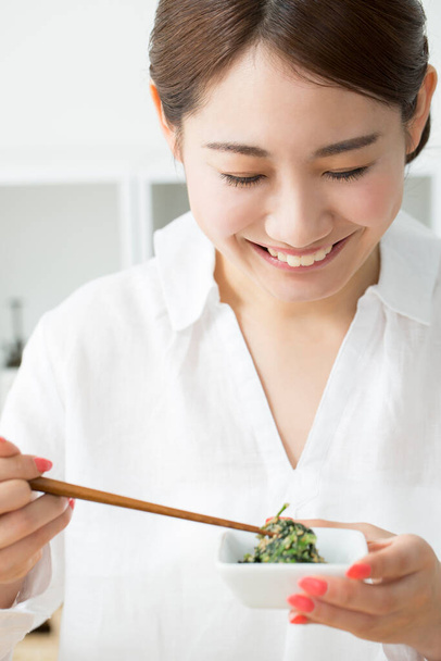 Asian woman eating food with chopsticks at home - Zdjęcie, obraz