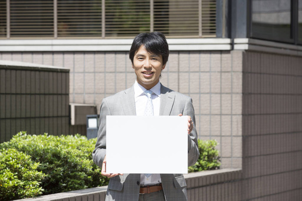handsome professional asian businessman holding blank placard and smiling at camera on street  - Photo, Image
