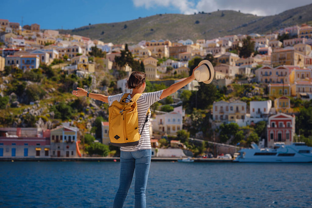 Sırt çantalı mutlu Asyalı kadın Symi Adaları 'nda tatilinin tadını çıkarıyor. Liman manzarası, Yunanistan 'ın Dodecanese kentindeki küçük bir ada, sakin bir atmosfer ve muhteşem bir mimari.. - Fotoğraf, Görsel