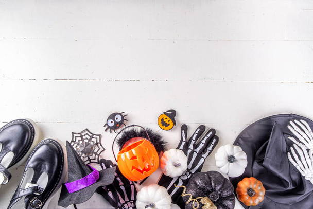 Los preparativos para la fiesta de Halloween de los niños, truco o tratar la tradición. Tradicional traje de Halloween para niños bruja, fantasma, esqueleto, accesorios de calabaza, con cubo de caramelo, decoración sobre fondo blanco - Foto, imagen