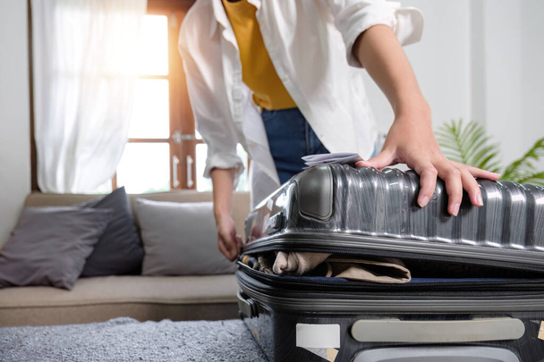 Женщина пытается закрыть чемодан, полный вещей в рамках подготовки к поездке.. - Фото, изображение