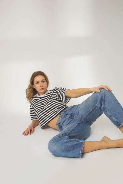 Modeporträt einer jungen Frau in entspannten weiten Jeans und gestreiftem T-Shirt auf weißem Hintergrund - Foto, Bild