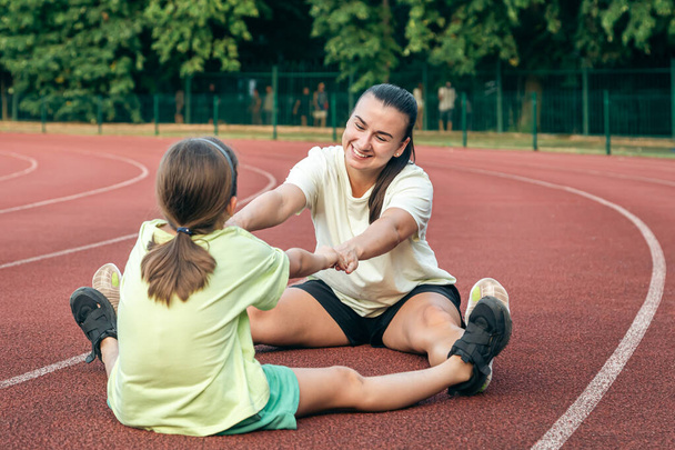 Mother and daughter go in for sports outdoors, caucasian woman and little girl are engaged in fitness at the stadium. - Photo, Image