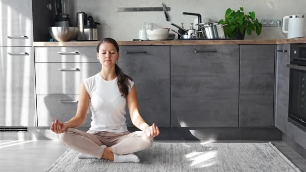 A fiatal nő ül és meditál a konyhában lévő koszos edények hátterén. Lassú, öngondoskodó, lassú életfelfogású. Kiváló minőségű 4k felvételek - Felvétel, videó