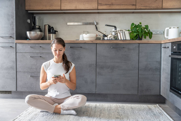 Fiatal nő ül egy telefont a háttérben piszkos edények a konyhában, lassítás, lassú élet, halogatás, halogatás koncepció. Kiváló minőségű fénykép - Fotó, kép