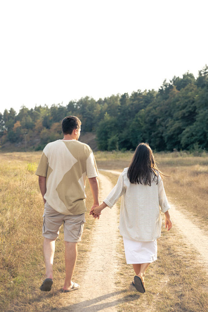 Egy férfi és egy nő sétálnak a mezőn, fogják egymás kezét, egy boldog család, egy szerelmes pár sétál, hátulról néznek.. - Fotó, kép