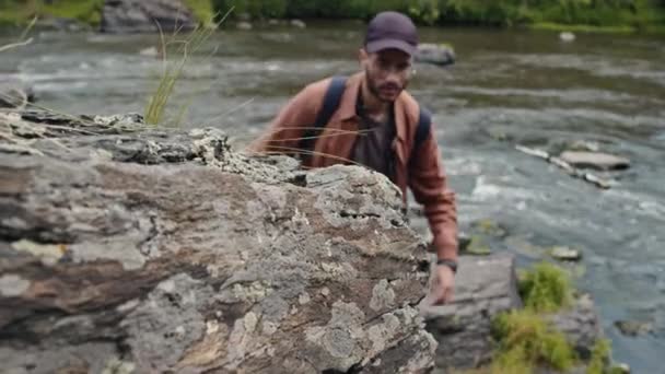 Shallow focus of young Biracial male tourist climbing mountain and touching stone - Footage, Video